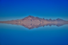 A distant rocky mountain reflects on water covering the Bonneville Salt Flats.